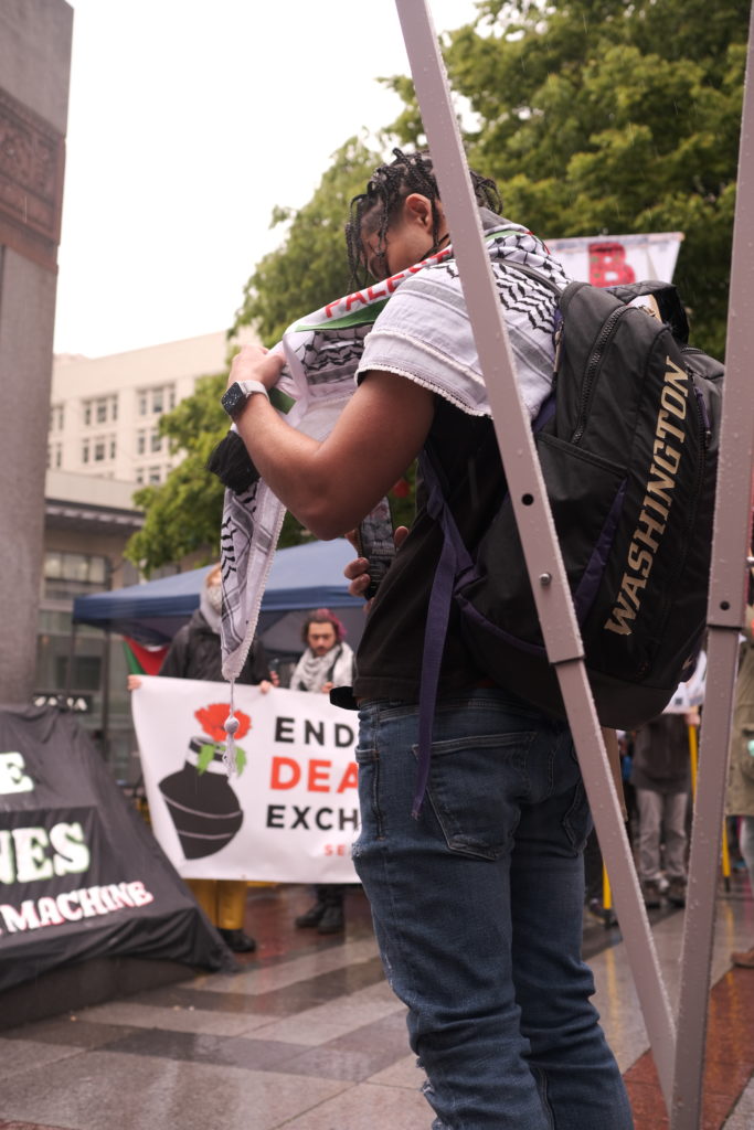 One protestor uses his keffiyeh to protect his phone from the rain as he streams the event. A keffiyeh is a traditional Arabian headdress made of cotton, initially used to protect from the sun and sand, it is now a symbol of Palestinian nationalism.
